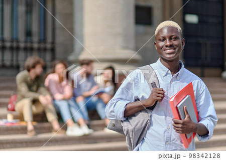 proud student with a textbook standing in front of the university. 98342128