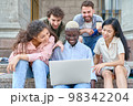 group of students with laptops sit on the steps near the campus. 98342204