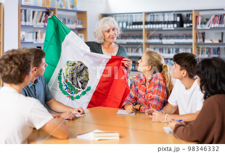 Mature female teacher shows scholchildren the national flag of Mexico 98346332
