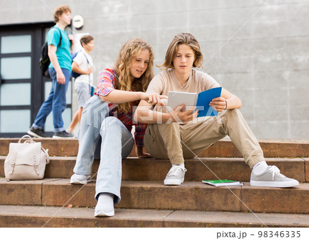 Teenagers doing homework on stairs outdoors 98346335