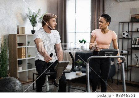 Young couple doing cardio on stationary bike and treadmill. Young couple doing cardio on stationary bike and treadmill. 98346551