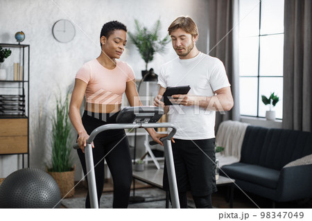 Fitness caucasian man trainer using tablet to show online lesson for african american woman 98347049