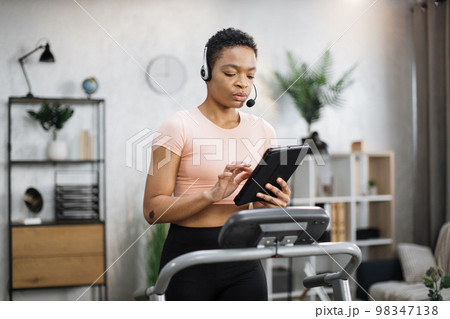Confident muscular sporty businesswoman in headset working remote from home using digital tablet 98347138