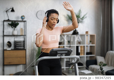 African american women with short curly hair in sports clothes and sneakers, listening music 98347205