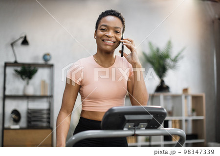 Young african american female in pink t-shirt jogging on treadmill Young african american female in pink t-shirt jogging on treadmill 98347339