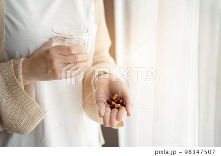 Depressed woman holding a glass of water, suffering from headaches, fighting stress with antidepressants, close-up view. Depressed woman holding a glass of water, suffering from headaches, fighting stress with antidepressants, close-up view. 98347507