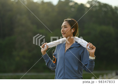 Portrait of sporty woman in sportswear and with towel resting after jogging in a green park on a sunny day Portrait of sporty woman in sportswear and with towel resting after jogging in a green park on a sunny day 98347833