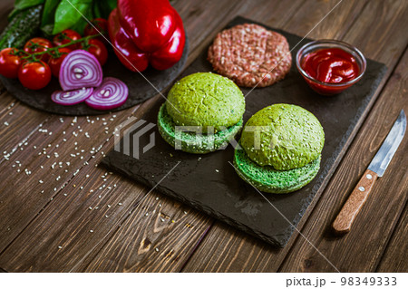 From above view of hamburger ingredients on the wooden table. Green buns for burger. Selective focus From above view of hamburger ingredients on the wooden table. Green buns for burger. Selective focus 98349333