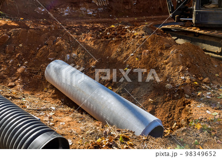 Worker laying sewage pipes in ground, preparing to put concrete pipes underground 98349652