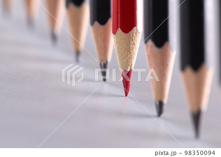 Red pencil stands out from crowd of many identical black pencils 98350094