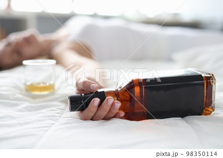 Woman is lying in bed dead drunk holding almost empty bottle of booze 98350114