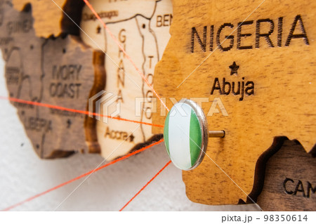 Nigeria flag on the pushpin with red thread showed the paths of movement or areas of influence in the global economy on the wooden map. Planning of traveling or logistic concept. Network connection. Nigeria flag on the pushpin with red thread showed the paths of movement or areas of influence in the global economy on the wooden map. Planning of traveling or logistic concept. Network connection. 98350614