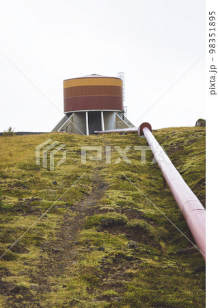 Vertical photo - red tube filled with hot water going up the green hill in Iceland 98351895