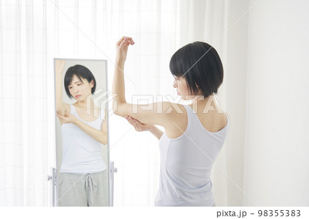 鏡の前で二の腕の贅肉を摘む女性 98355383