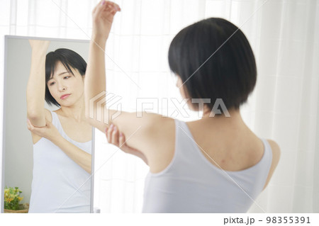 鏡の前で二の腕の贅肉を摘む女性 鏡の前で二の腕の贅肉を摘む女性 98355391