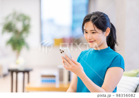 リビングでスマートフォンを操作する若い女性。 98356082