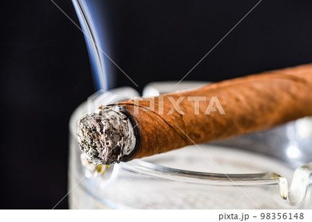 Lighting cuban cigar dark background. Tobacco smoking. Tobacco smoke. Nicotine addiction. Steaming cigar 98356148
