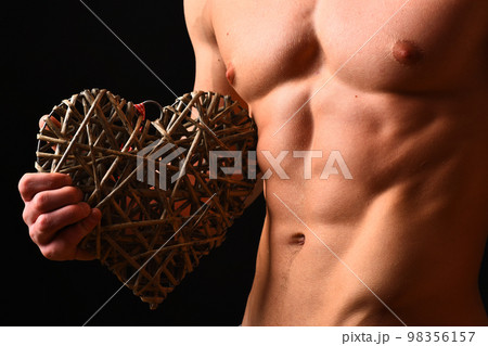 Athletes body in close up, hand holding big rattan heart Athletes body in close up, hand holding big rattan heart 98356157