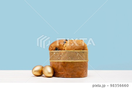Happy Easter banner. Italian Easter Decorated Panettone and golden eggs on white table. Wide banner on blue. 98356660