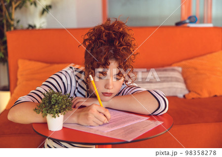 Young girl writing something and looking tired and bored Young girl writing something and looking tired and bored 98358278