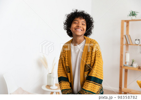 Beautiful african american girl with afro hairstyle smiling at home indoor. Young african woman with curly hair laughing in living room. Freedom happiness carefree happy people concept 98358782