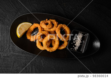 fried squid rings in breadcrumbs with lemon and soy sauce on black concrete background fried squid rings in breadcrumbs with lemon and soy sauce on black concrete background 98360014