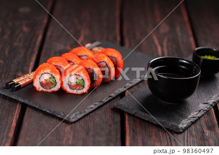 California sushi roll with salmon crab, cucumber and tobiko caviar served on black board close-up - Japanese food California sushi roll with salmon crab, cucumber and tobiko caviar served on black board close-up - Japanese food 98360497