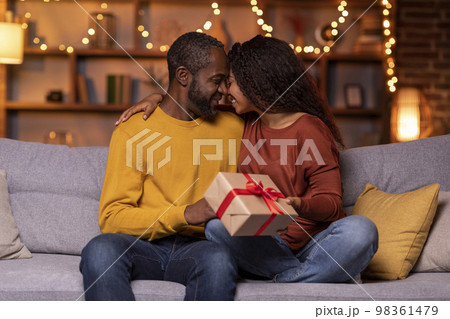 Loving black man and woman holding gift box, home interior Loving black man and woman holding gift box, home interior 98361479