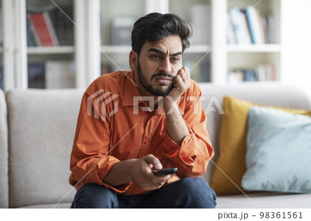 Bored middle eastern guy sitting at home, switching tv Bored middle eastern guy sitting at home, switching tv 98361561
