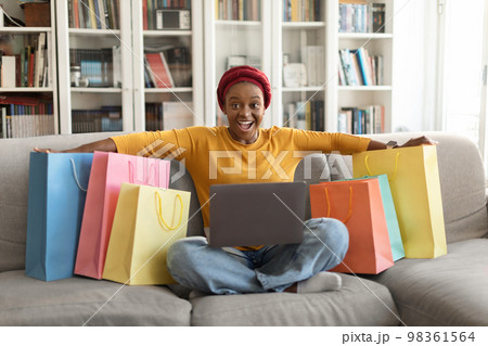 Happy black woman shopaholic sitting among purchases on couch 98361564
