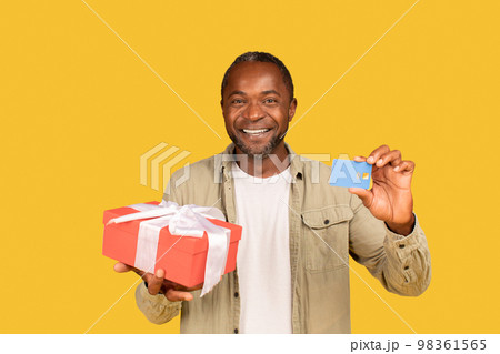 Cheerful african american middle aged man show gift box and credit card, recommend banking Cheerful african american middle aged man show gift box and credit card, recommend banking 98361565