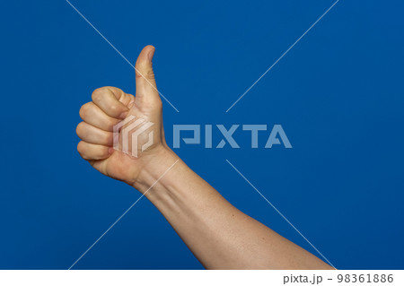 Thumb up hand sign. man's hand showing thumb up, like, ok, approval, accept, okay, good, positive hand gesture. Isolated on blue studio background. 98361886