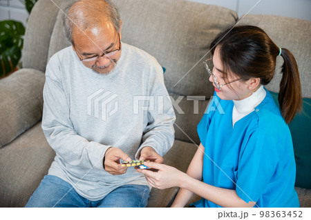 Asian nurse with physician explaining prescription medicine to attentive senior man at home, Doctor woman explain dosage pill old man, Healthcare worker caregiver visiting in house in living room 98363452