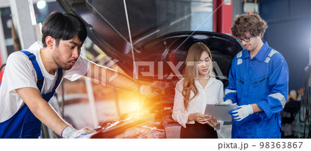 Man garage worker and woman customer talking to discuss the details of car repairs. Man garage worker and woman customer talking to discuss the details of car repairs. 98363867