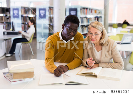 Friendly adult students preparing in library Friendly adult students preparing in library 98365554