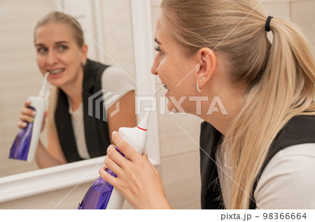 A woman with braces on her teeth uses an irrigator. Close-up portrait. A woman with braces on her teeth uses an irrigator. Close-up portrait. 98366664