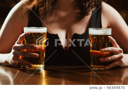 two glasses of light foam beer lager in the hands of a woman with big sexy breasts at the bar 98369870