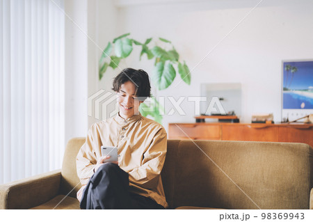 ソファに座ってスマホを見る男性 98369943