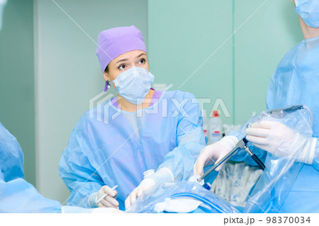 Portrait of a young beautiful woman surgeon in a mask and surgical uniform 98370034