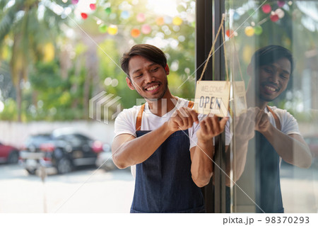 Young male manager in restaurant with tablet. Man coffee shop owner with open sign. Small business concept 98370293