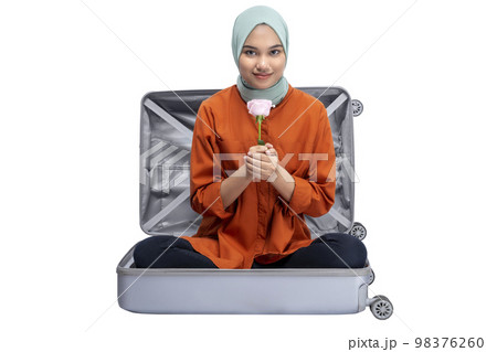 Asian Muslim woman in a headscarf sitting in a suitcase while holding a pink rose flower Asian Muslim woman in a headscarf sitting in a suitcase while holding a pink rose flower 98376260