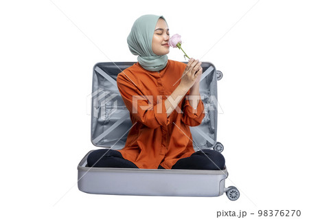 Asian Muslim woman in a headscarf sitting in a suitcase while holding a pink rose flower Asian Muslim woman in a headscarf sitting in a suitcase while holding a pink rose flower 98376270