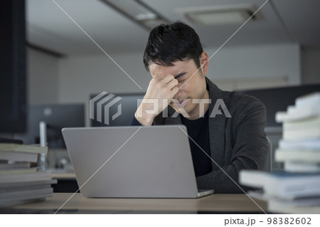 デスクのノートパソコンの前で頭を抱える30代のビジネスマン デスクのノートパソコンの前で頭を抱える30代のビジネスマン 98382602