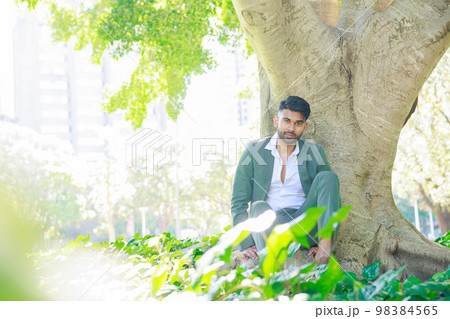 大きな樹の下に座るスーツを着たインド人男性 98384565