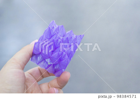 Person holding a abstract model printed on a 3D printer from purple plastic on his hand on gray background close-up. Concept modern printing technology Person holding a abstract model printed on a 3D printer from purple plastic on his hand on gray background close-up. Concept modern printing technology 98384571
