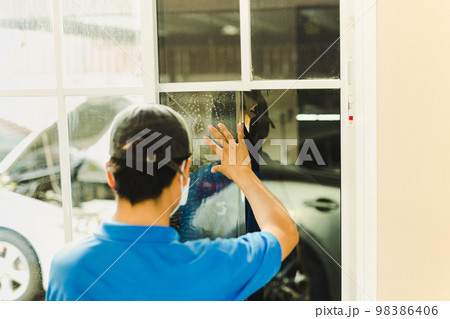 Woker wrapping tinting a house window with tinted foil. 98386406