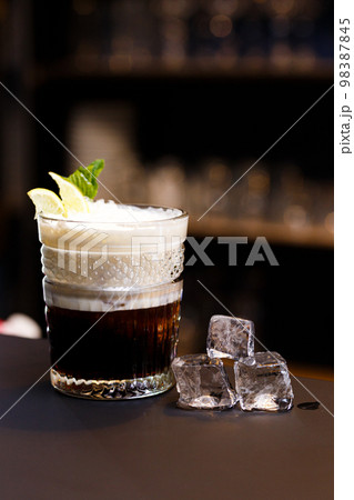 On a bar counter and a dark background. Alcoholic cocktail with ice. 98387845