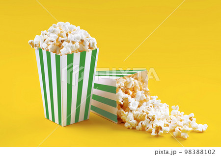 Two green white striped carton buckets with tasty cheese popcorn, isolated on yellow background Two green white striped carton buckets with tasty cheese popcorn, isolated on yellow background 98388102