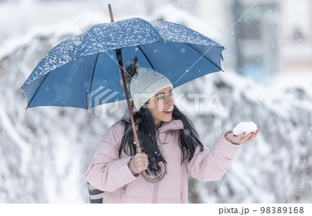 Happy woman holding an umbrella on a cold snowy day and holding fresh snow in her hand 98389168