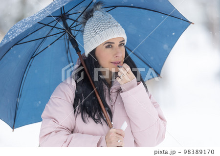 Gorgeous brunette puts on lip balm dressed in warm clothes outdoors on a cold winter day 98389170